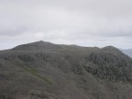 A busy Scafell Pike summit seen from an empty Scafell