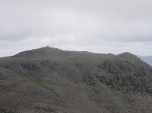 A busy Scafell Pike summit seen from an empty Scafell
